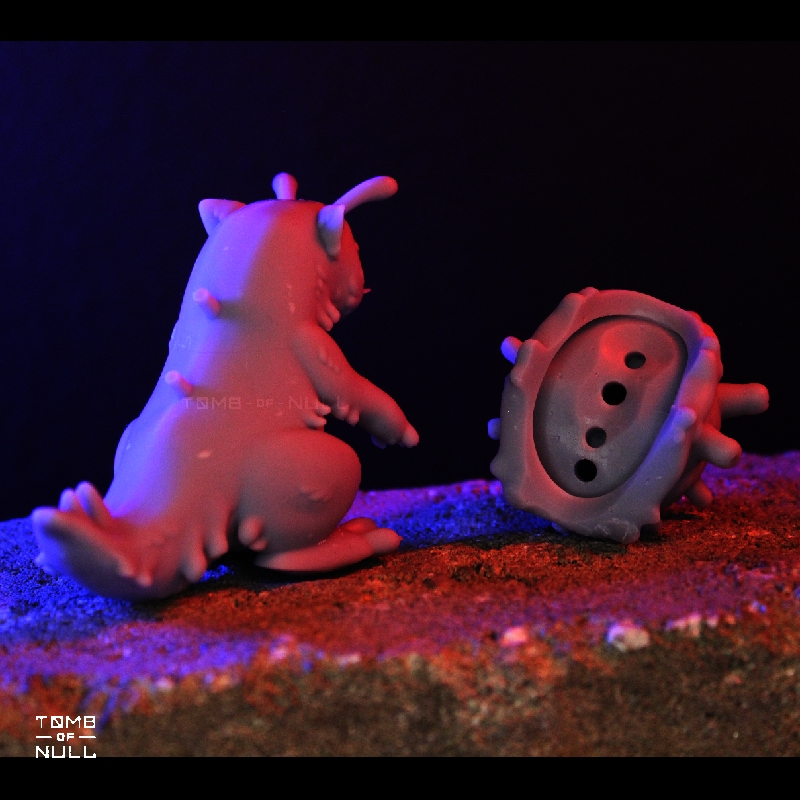 A photo of a snail-cat kaiju sculpture in a middle grey color. Their shell is detacted from their body, showing the peg-in-hole design that is used to affix the shell to the body of the sculpt.