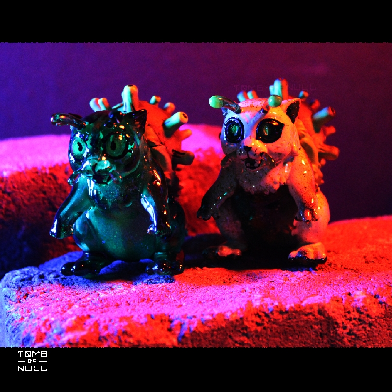 A photo of two snail-cat kaiju sculptures, one cream and green and in dark green.