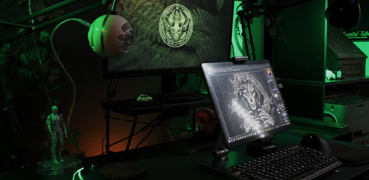 Photo of a desk with digital drawing tools set up, including a computer with extra screen. On the screen is a digital illustration of a lich queen in progress.